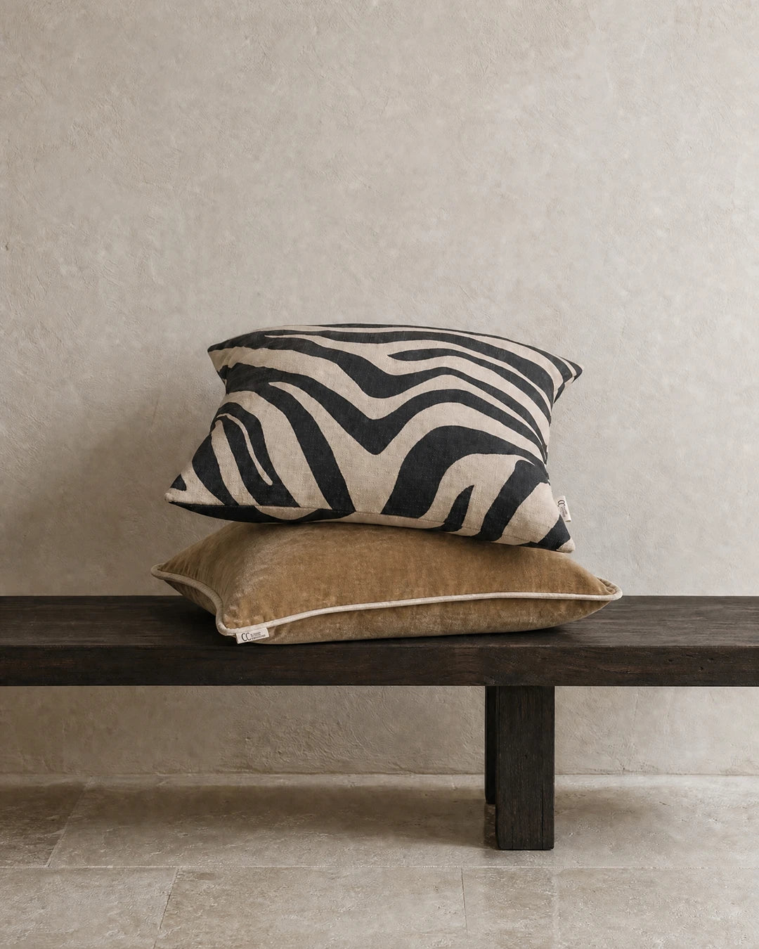 Kuddar 50x50 cm från Classic Collection: Savannah Svart/Beige med grafiskt mönster och Velvet Stonewash Guld i tvättad bomullssammet, placerade på en mörk träbänk.
