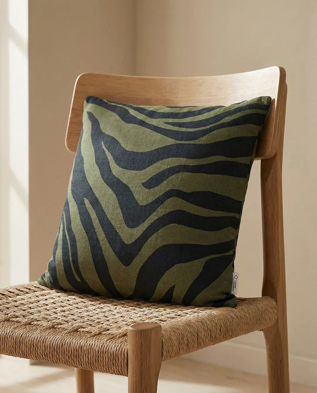 Square olive green linen throw pillow with black zebra stripe pattern on a wooden chair.