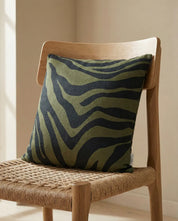 Square olive green linen throw pillow with black zebra stripe pattern on a wooden chair.