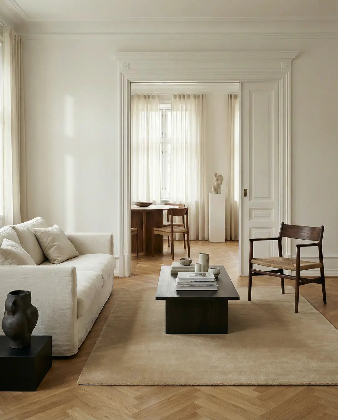 Minimalist living room with cream sofa, dark wood coffee table, and accent chair on a herringbone floor.