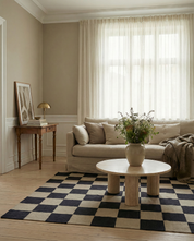 Moderner Wohnbereich mit kariertem Teppich, rundem Travertin-Couchtisch und beigem Leinensofa in hellem Ambiente.