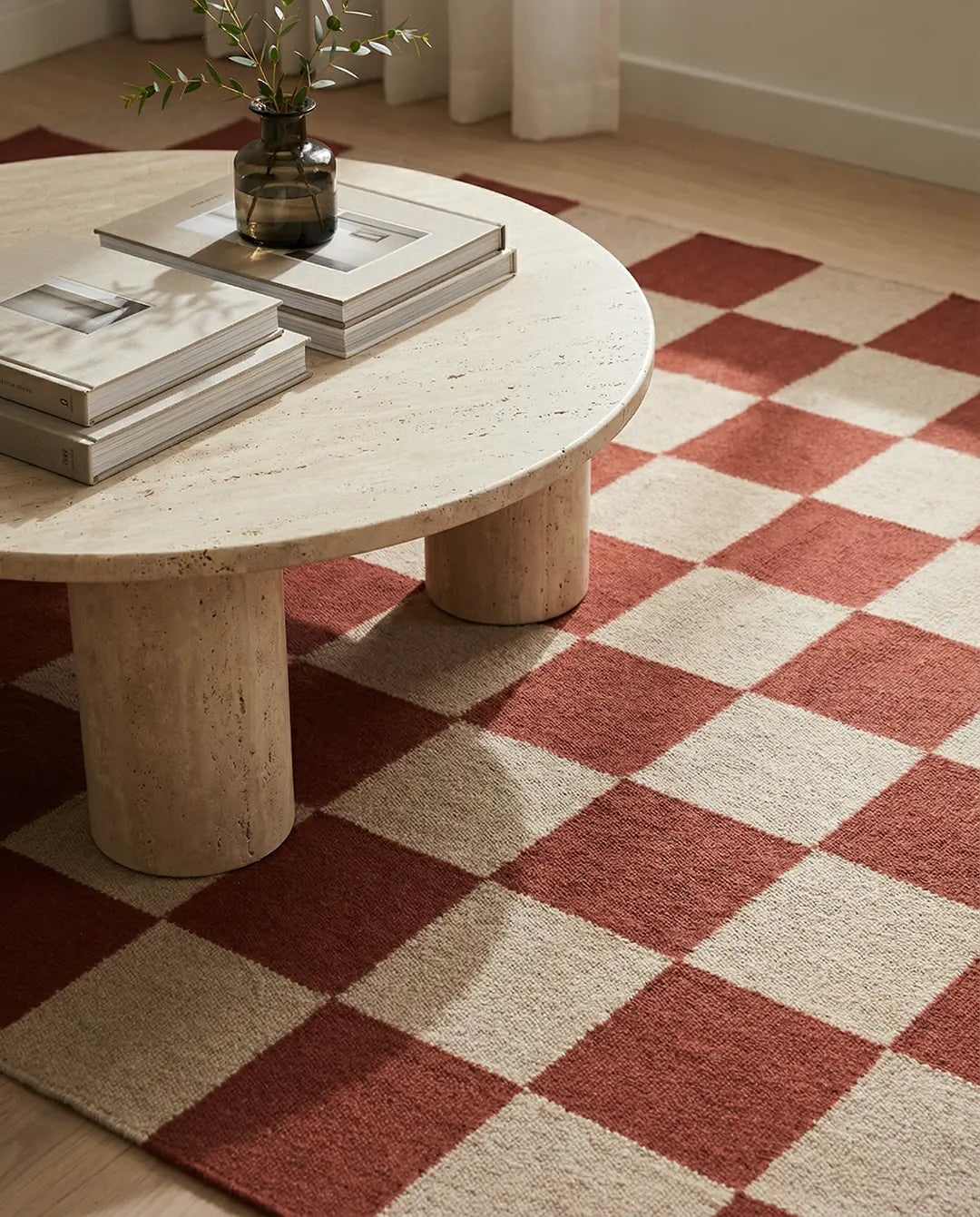Runder Travertin-Couchtisch auf einem beigen und rostroten Schachbrett-Teppich im modernen Wohnzimmer.