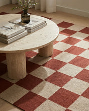 Runder Travertin-Couchtisch auf einem beigen und rostroten Schachbrett-Teppich im modernen Wohnzimmer.