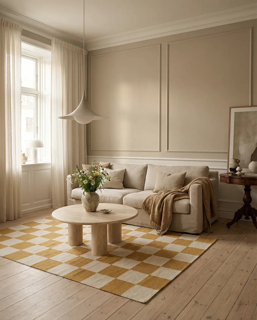 Beiger runder Couchtisch aus Travertin in einem Wohnzimmer mit gelb-weißem Schachbrett-Teppich und beigem Sofa.