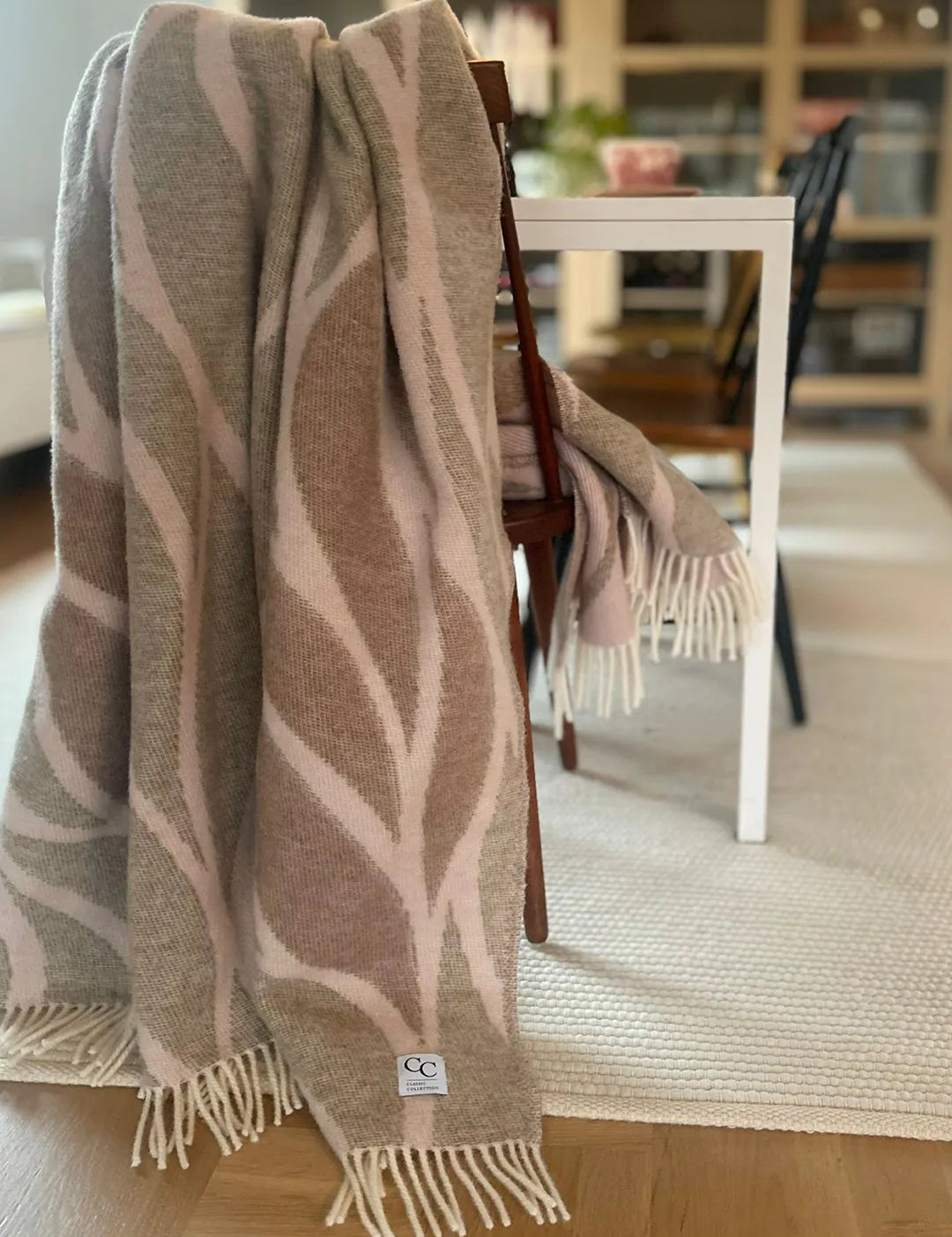 Pläd Folia Pink i NZ-ull, hängd över en stol vid ett matbord i ett vardagsrum.