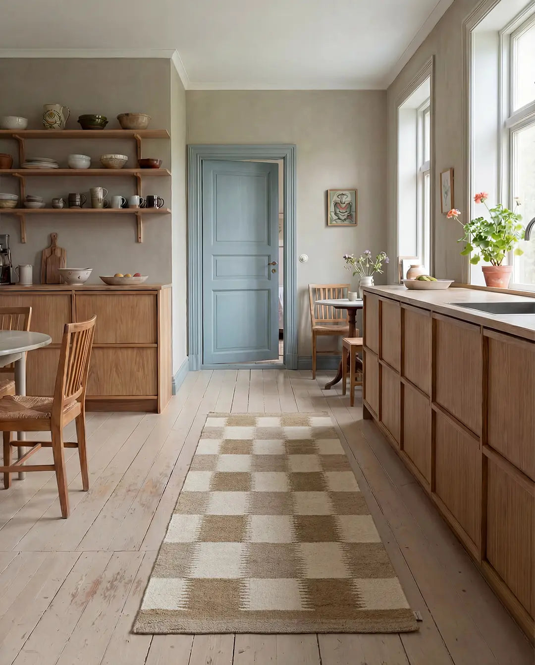 Rutig beige och vit matta i ett ljust kök med trämöbler och en blå dörr.