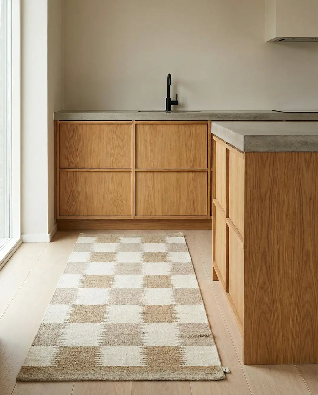 Beige och vit rutig matta med vävd textur placerad på golvet i ett modernt kök med träluckor och betongbänkskiva.