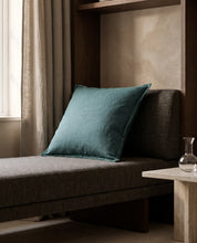 Kuddfodral Classic Linen Teal 50x50 cm från Classic Collection i enfärgat linne, stylat på en mörk stoppad bänk i en varm, elegant interiör.