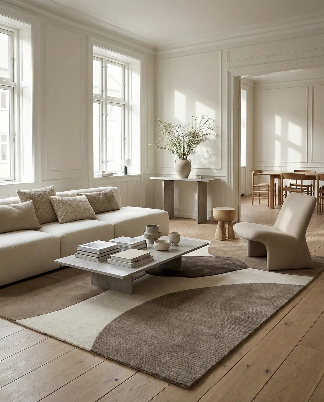 Modern living room with a beige sofa, sculptural lounge chair, and a large area rug featuring organic, abstract brown shapes.