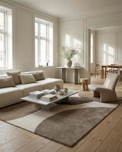 Modern living room with a beige sofa, sculptural lounge chair, and a large area rug featuring organic, abstract brown shapes.