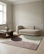Designer-Teppich mit abstraktem, buntem Muster in organischen Formen vor einem modernen beigen Sofa im Wohnzimmer.