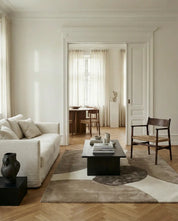 Minimalist living room featuring a beige linen sofa, dark wood coffee table, and abstract geometric patterned area rug.