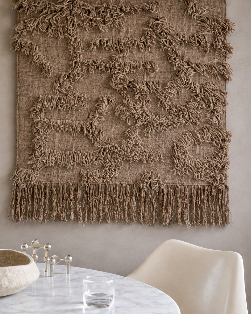 Rio Beige väggbonad, 100 × 100 cm, handvävd i ull, upphängd på vägg ovanför runt bord i ljus interiör