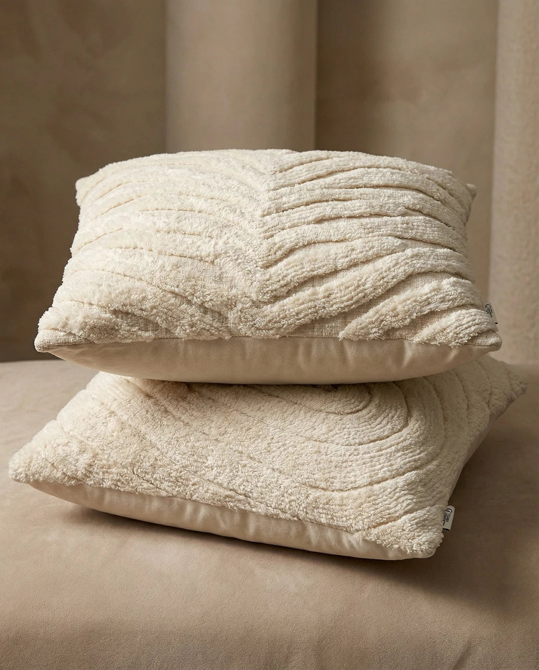 Two cream-colored throw pillows with textured, tufted patterns stacked on a matching neutral surface.