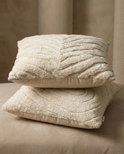 Two cream-colored throw pillows with textured, tufted patterns stacked on a matching neutral surface.