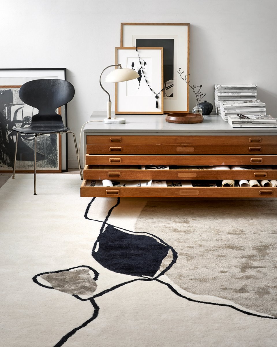 Cremefarbener Designer-Teppich mit abstraktem schwarzen Linienmuster und grauen Akzenten im modernen Wohnzimmer.