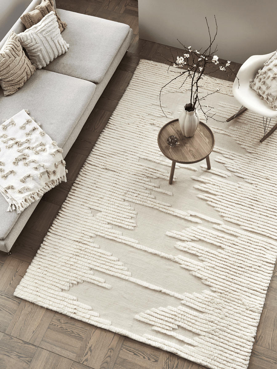 Cream-colored area rug with a textured geometric pattern in a modern living room setting.