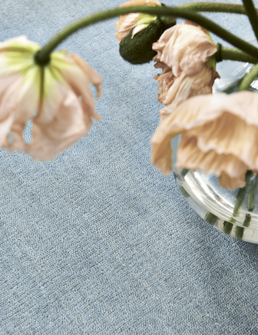 Handvävd ullmatta Solid Blå, detaljbild med mycket dagsljus och blommor i korall-färg som syns i förgrunden.