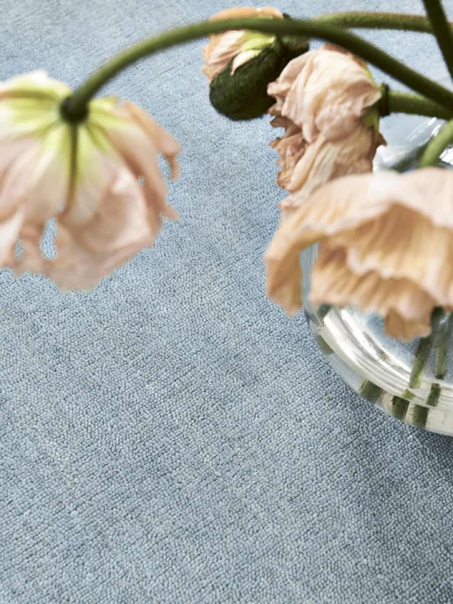 Handvävd ullmatta Solid Blå, detaljbild med mycket dagsljus och blommor i korall-färg som syns i förgrunden.