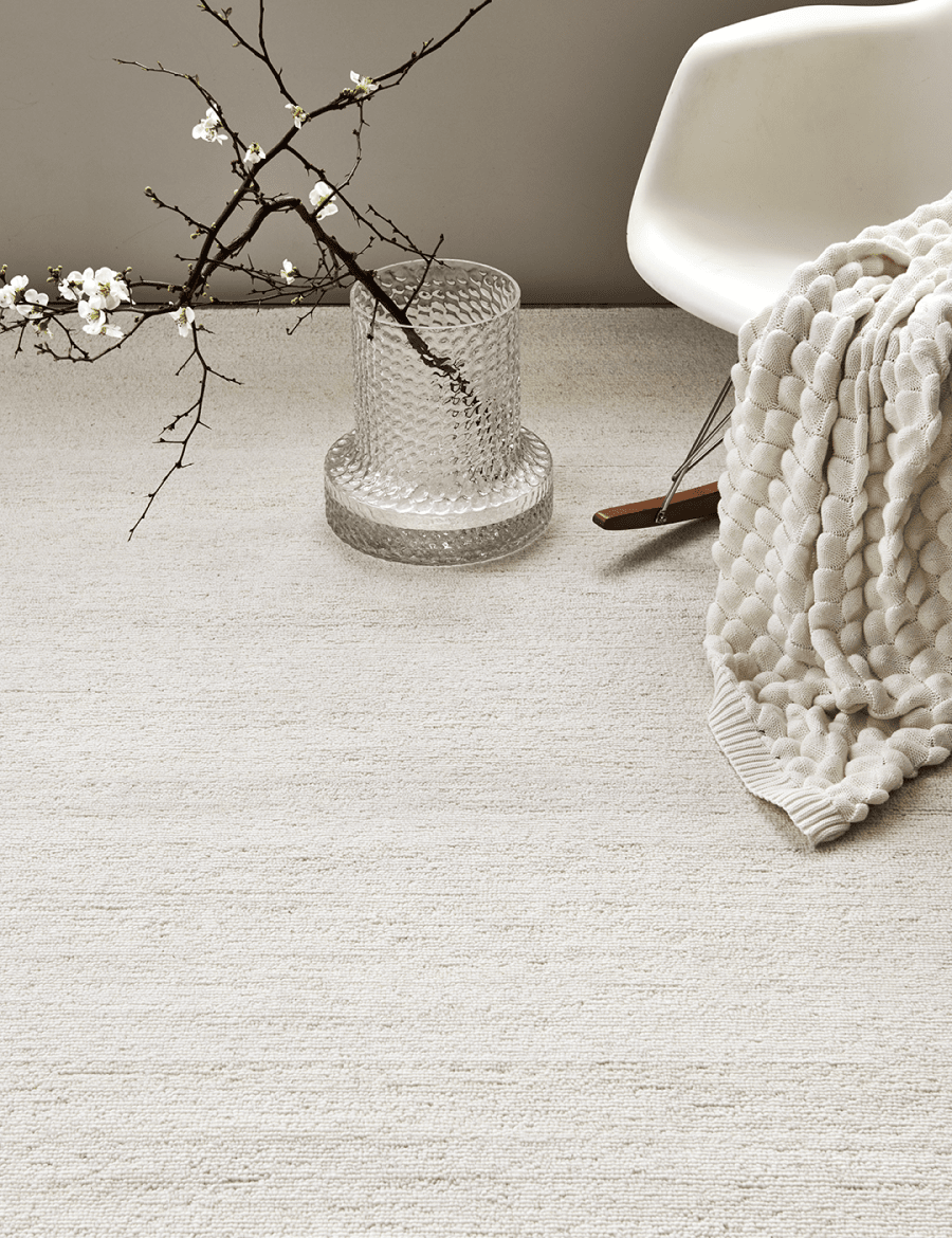 Textured cream area rug in a cozy living room with a white rocking chair, knitted throw, and glass vase with blossoms.