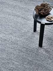 Blue textured wool loop pile area rug with a small black side table and dried botanical decor.