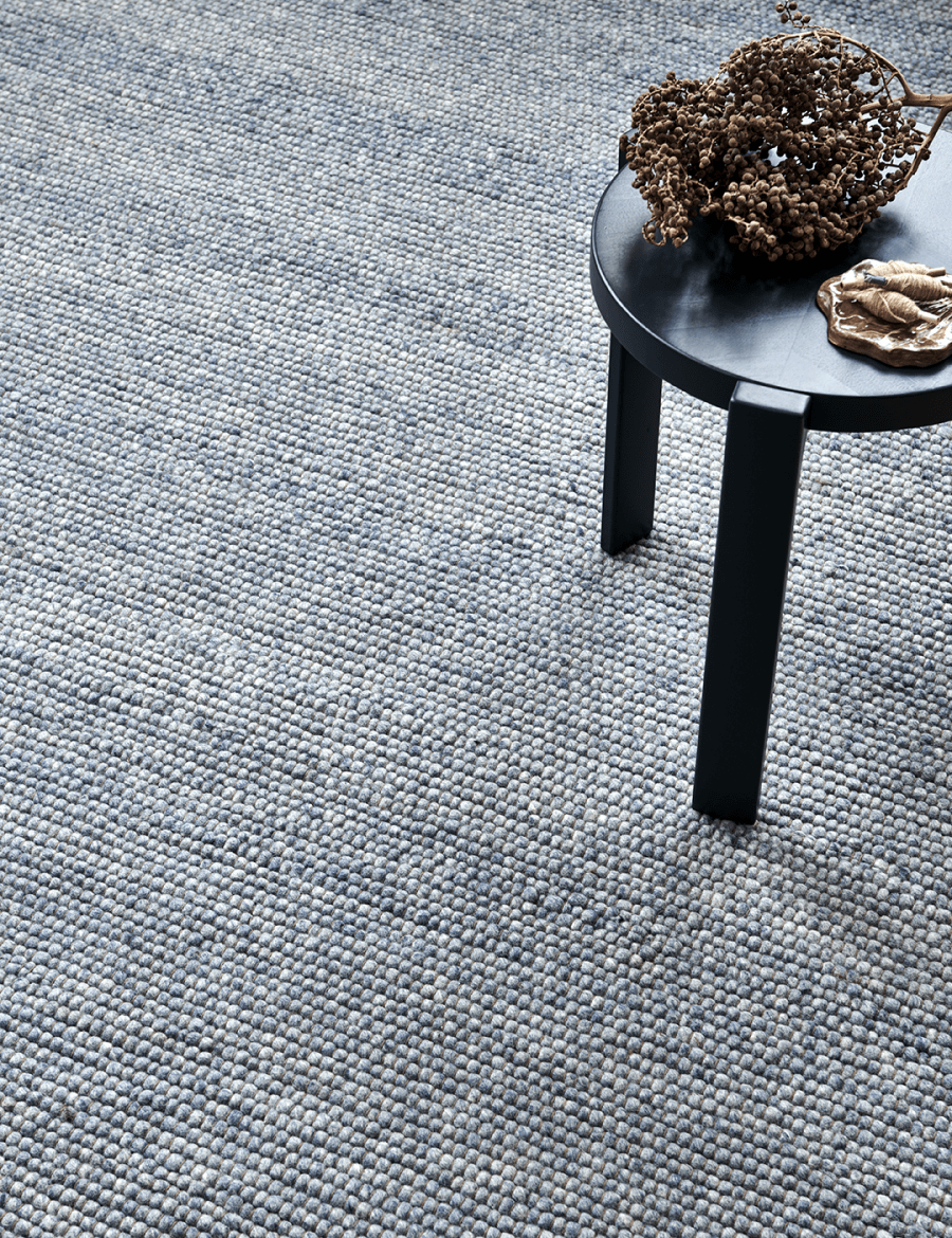 Textured blue wool rug with a chunky, hand-knotted bobble pattern next to a black stool.