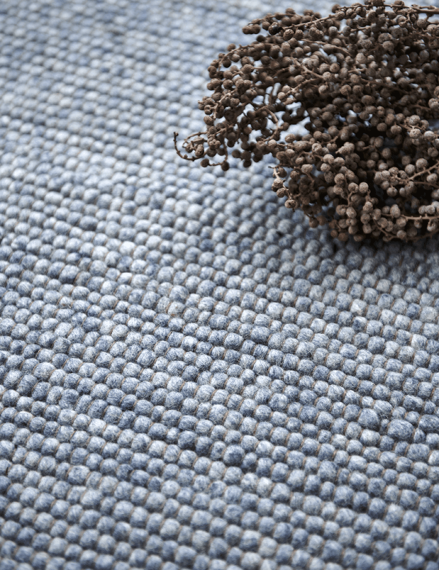 Textured grey wool pebble-style area rug with a decorative dried floral accent.