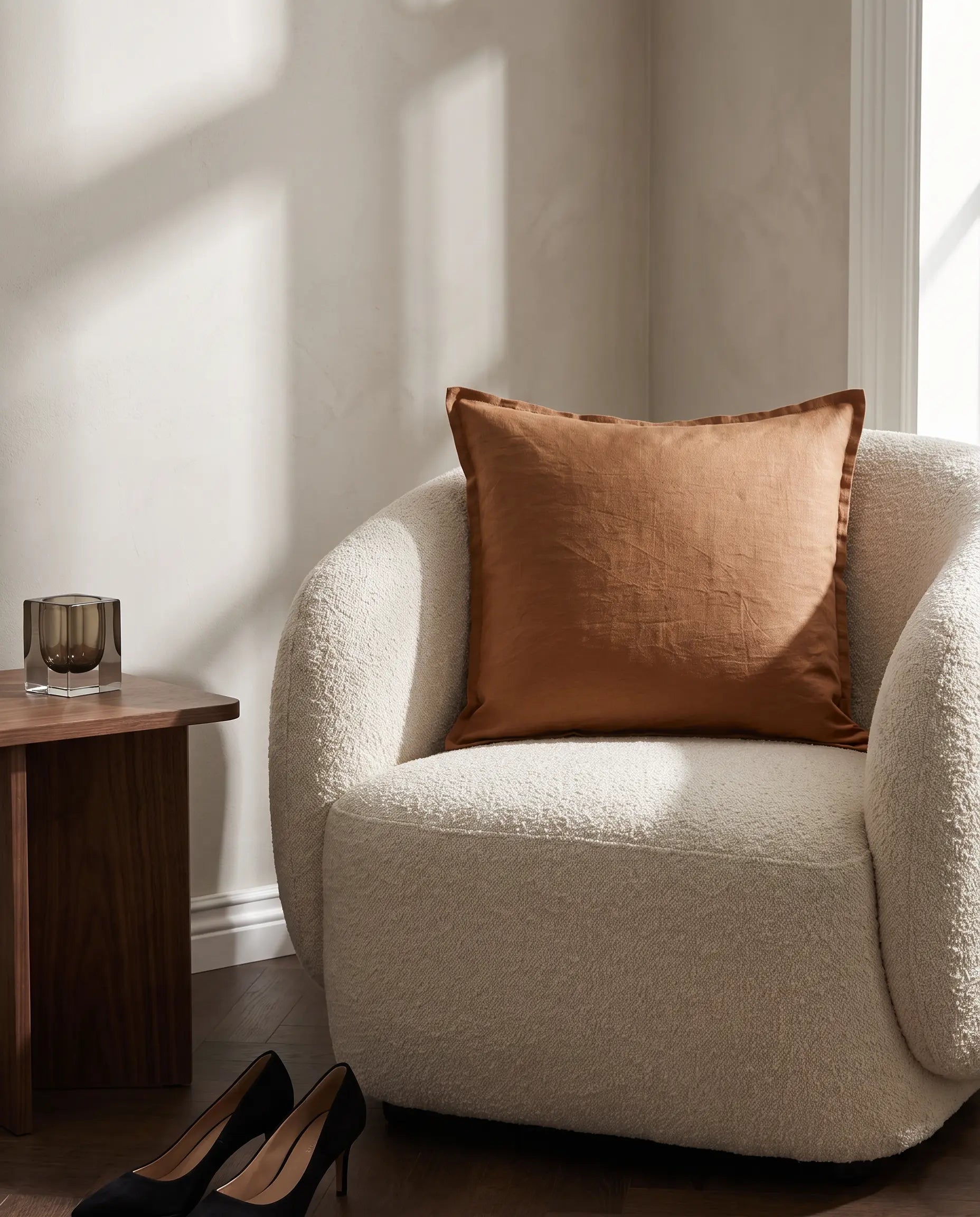 Kuddfodral Classic Linen Terracotta 50x50 cm från Classic Collection i enfärgat linne, stylat i en ljus fåtölj i en varm, neutral interiör.