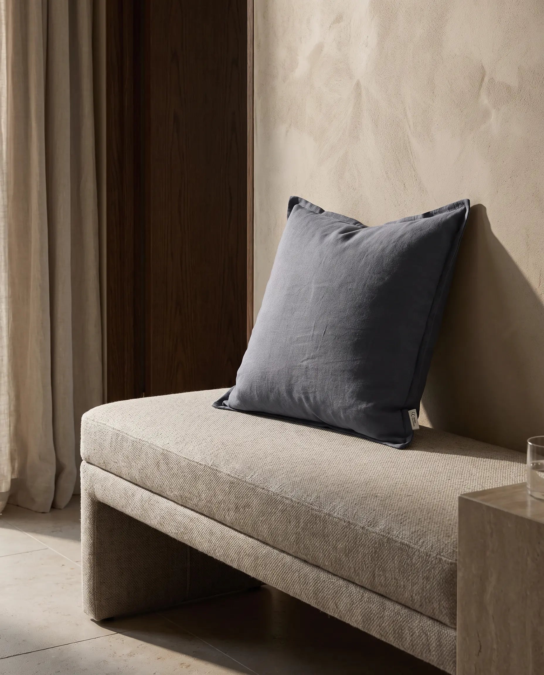 Kuddfodral Classic Linen Midnattsblå 50x50 cm från Classic Collection i enfärgat linne, stylat på en ljusbeige bänk i en varm, neutral interiör.