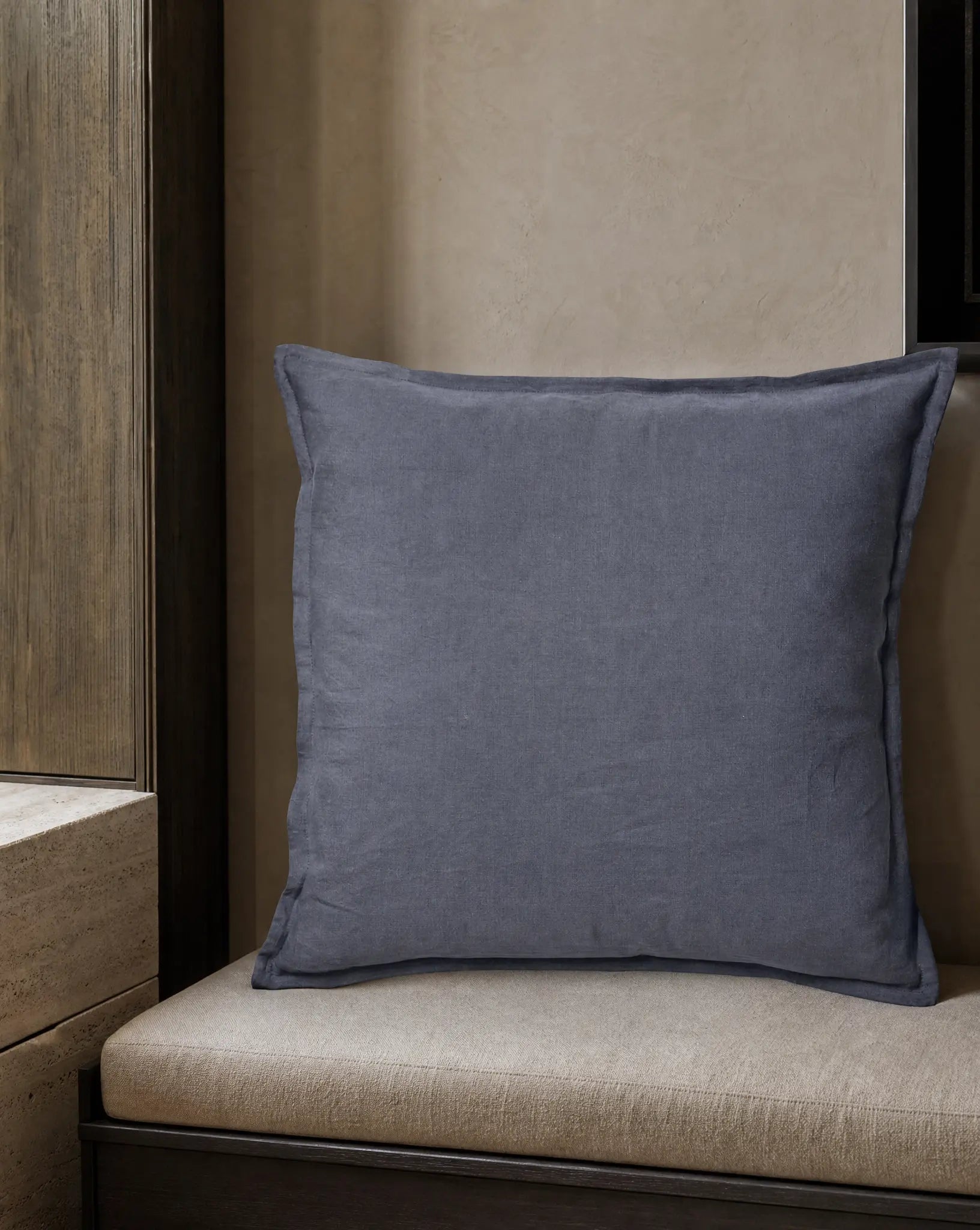 Kuddfodral Classic Linen Midnattsblå 50x50 cm från Classic Collection i enfärgat linne, stylat på en ljusbeige bänk i en varm, neutral interiör.