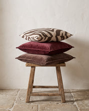 Kuddar 50x50 cm från Classic Collection: Savannah i off-white och brun samt Classic Velvet i burgundy och brun, arrangerade på en träpall med patina.