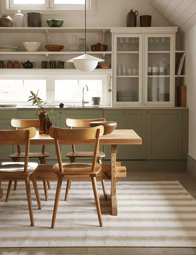Kitchen featuring wooden chairs, a matching dining table, and a neutral-toned striped area rug on a tiled floor.