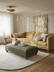 Senfgelbes Sofa mit grauem Polsterhocker in einem hellen, gemütlich eingerichteten Wohnzimmer.