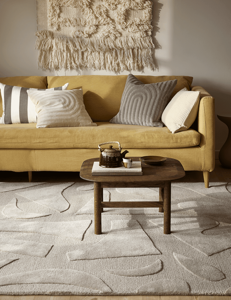 Beige Wohnzimmer mit gelbem Sofa, gemustertem Teppich, Holztisch und Wandbehang aus Wolle im modernen Stil.