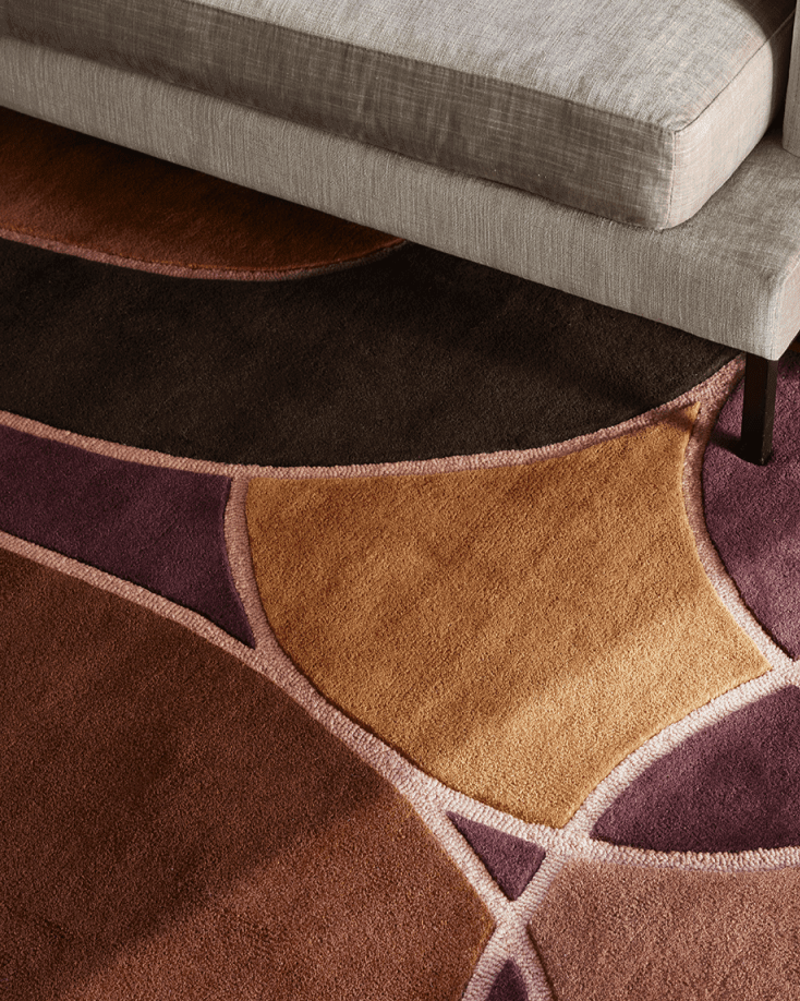 Teppich mit abstraktem, geometrischem Muster in Brauntönen und Lila, mit weicher Textur unter einem beigen Sofa.