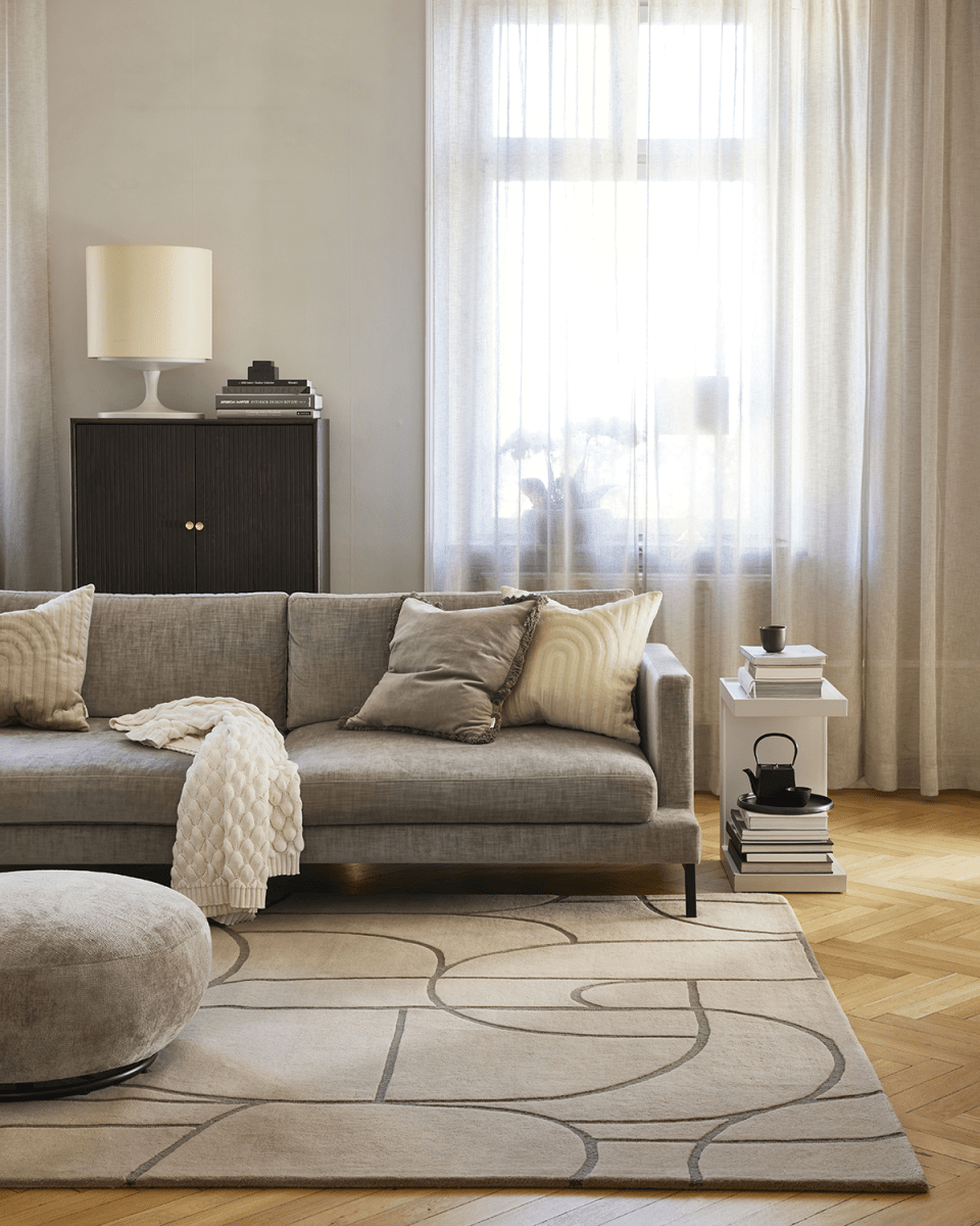 Beiger Teppich mit abstraktem, geschwungenem Linienmuster in einem modernen, hellen Wohnzimmer mit Sofa.