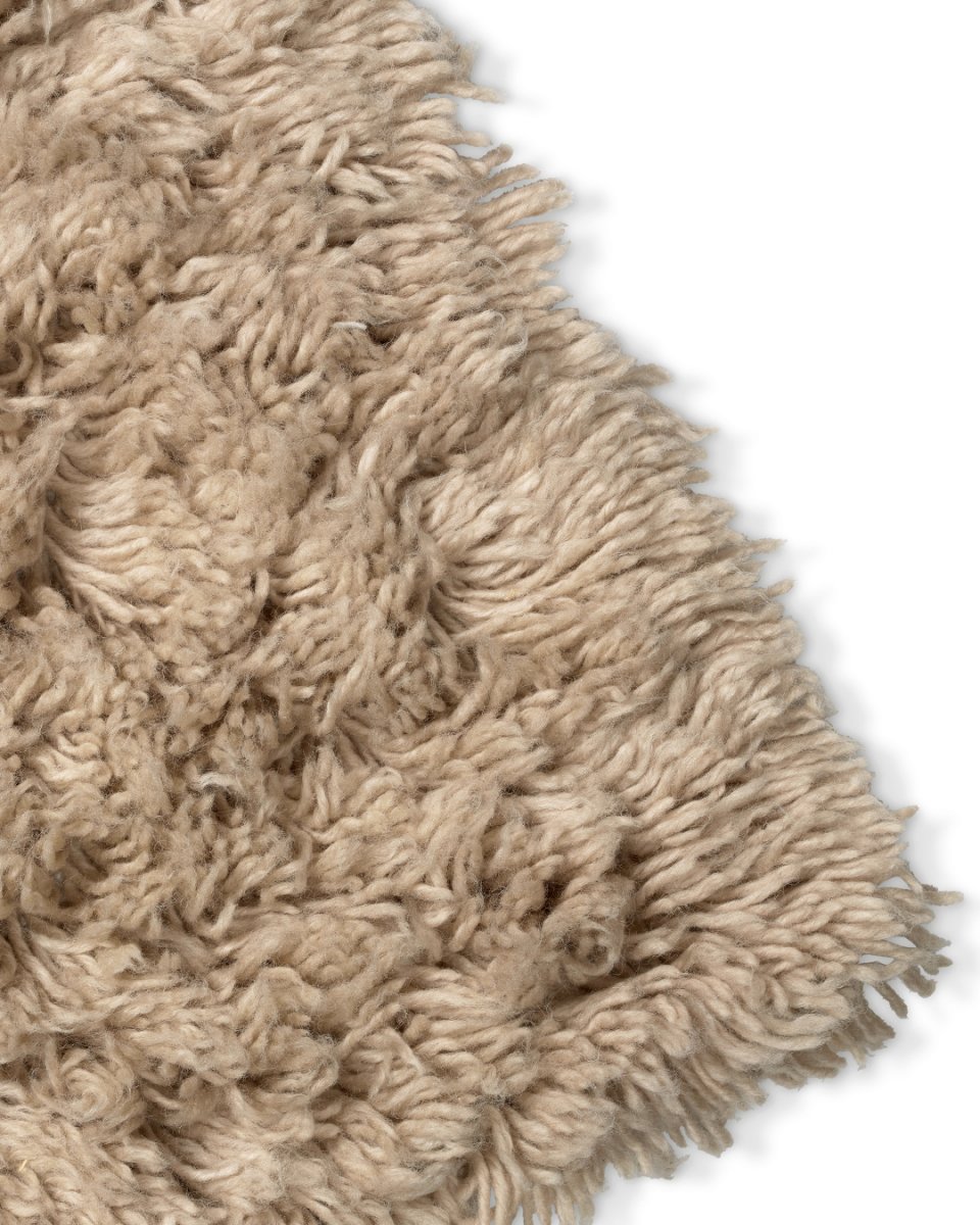 Close-up of a soft, beige shag area rug with a thick, textured pile and tasseled edge.