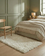 Fluffy cream-colored area rug in a modern bedroom with sage green paneled walls and a wooden chair.
