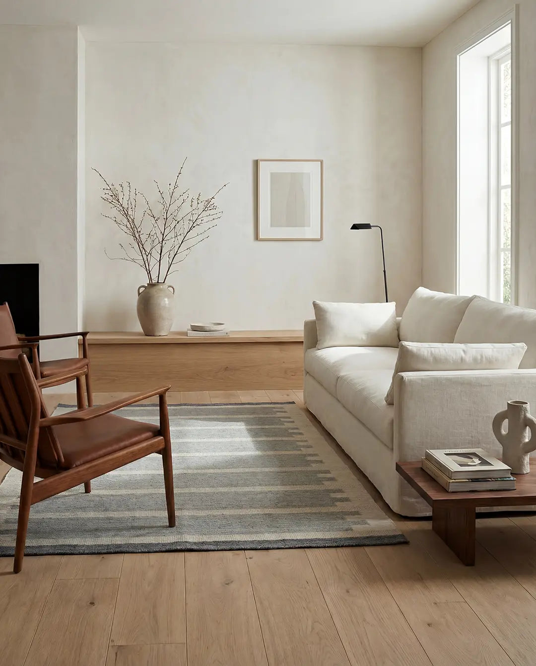 Vardagsrum med grå randig matta, ljus soffa och två läderfåtöljer i en stilren, minimalistisk inredning.