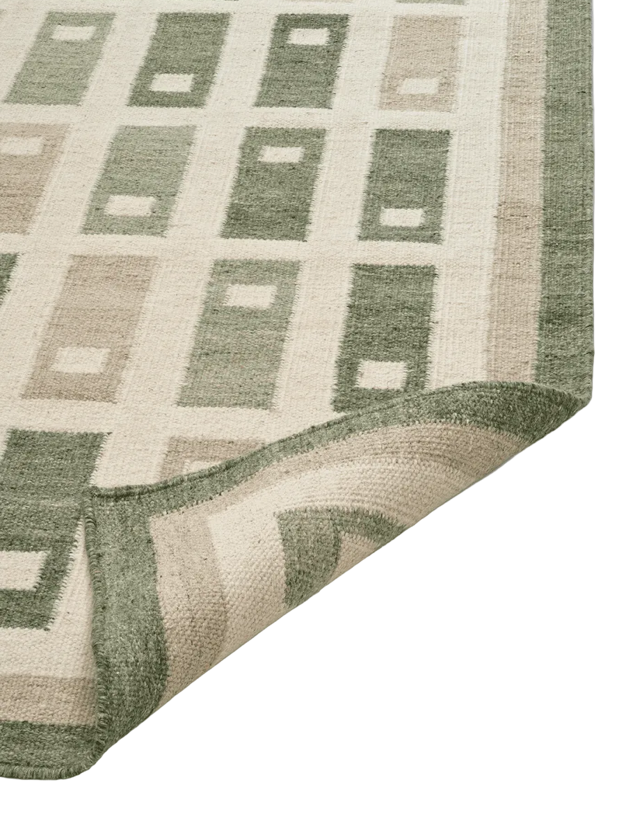 Fyrbo matta i ull med blockmönster i naturnära grönt och beige, flatvävd och vändbar, frilagd produktbild mot ljus bakgrund. Detaljbild av ett uppvikt hörn.