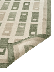 Fyrbo matta i ull med blockmönster i naturnära grönt och beige, flatvävd och vändbar, frilagd produktbild mot ljus bakgrund. Detaljbild av ett uppvikt hörn.