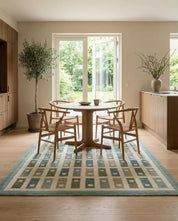 Moderner runder Holztisch mit vier Stühlen auf einem rechteckigen Teppich mit blau-grünem geometrischem Muster.