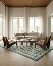 Modernes Wohnzimmer mit gebogenem beigen Sofa, zwei Holzsesseln mit Wiener Geflecht und einem geometrischen Teppich in Blau.