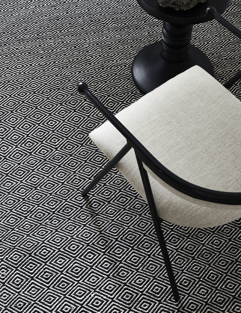 Moderner schwarz-weißer Teppich mit geometrischem Rautenmuster in einem minimalistisch eingerichteten Raum.