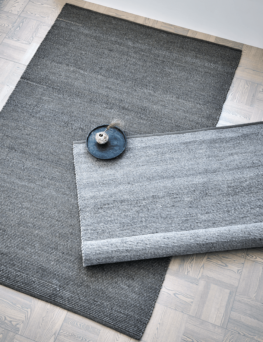 Dark grey woven area rug with a textured, modern looped finish layered on a light grey rug on a wooden parquet floor.