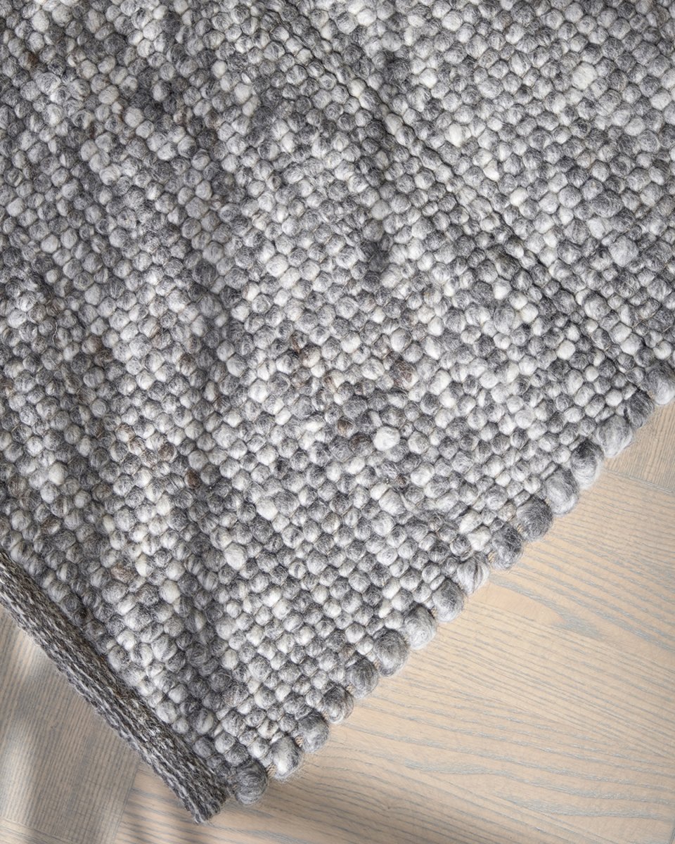 Grey wool area rug with a chunky, hand-knotted bobble texture on a light wood floor.