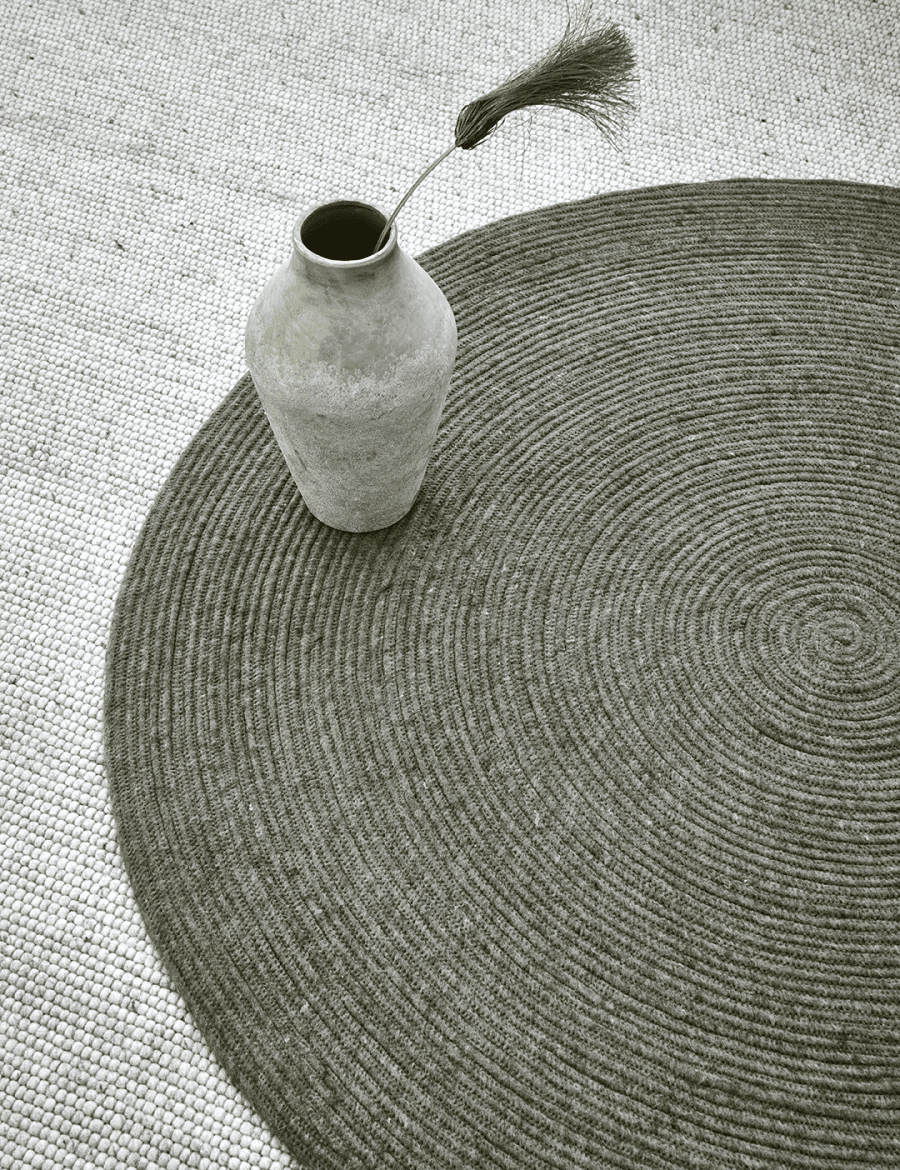 Dark grey circular braided jute rug with a textured spiral design on a light woven carpet background.