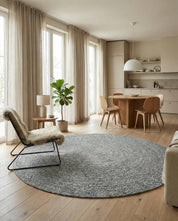 Runder, grauer Teppich aus grobem Strick in einem hellen, skandinavisch eingerichteten Wohn- und Esszimmer.