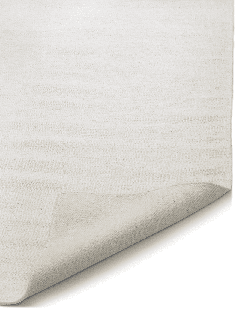 Minimalist solid white area rug with a folded corner revealing the textured cotton fabric weave.