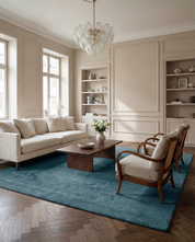 Beige soffgrupp med matchande fåtöljer och mörk träsoffbord på en stor, mjuk blå matta i ett elegant vardagsrum.
